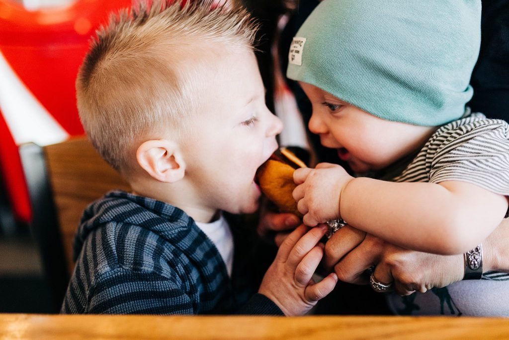 two small boys fight over a hot dog during a documentary photography session at Five Guys Burgers and Fries