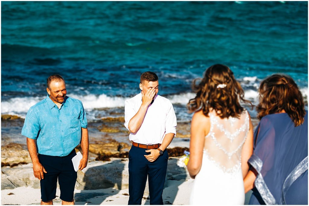 groom wipes tears from his eyes as he sees bride walk down the beach