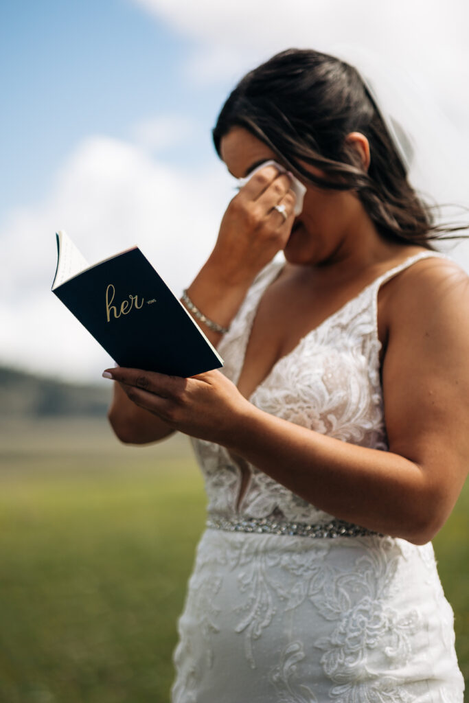 A bride wiping her eyes while she reads personalized vows during an intimate elopement in Teton National Park